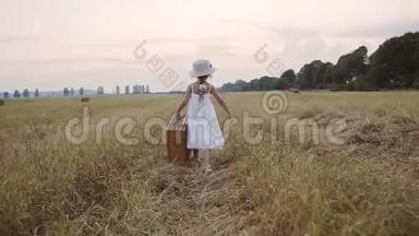 一个穿着白色连衣裙，头上戴着草帽的漂亮小女孩去田野迎接日落。 一个小女孩